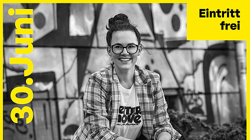 Eine Frau mit dunkler Brille lächelt ins Bild, sie trägt eine karierte Jacke