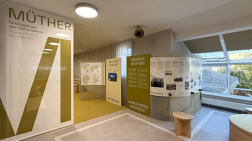 Ausstellungsraum mit Texttafeln und Monitor zur Ausstellung über Müther im Hyparforum, mit Sitzmöbeln und großen Fenstern im Hintergrund.
