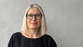 Judith Groß Die Person ist im Porträt vor einer Betonwand zu sehen.