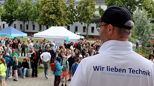 Über die Schulter eines Mannes blicktz man auf eine Menschenmenge.