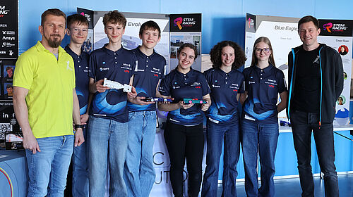STEM-Racing-Team 2025 Die drei Schülerinnen und drei Schüler des Teams stehen nebeneinander, eingerahmt von den Professoren. Sie tragen einheitliche dunkelblaue T-Shirts mit dem Teamnamen.