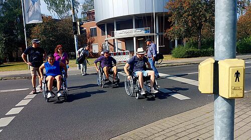 Eine Gruppe quert in Rollstühlen und zu Fuß eine Ampelanlage.