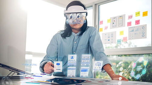 Introduction_Image_Symbolbild_WI_Master_SL_2023 Eine Frau mit AR Brille sieht vor sich virtuelle Tabs vor einem Tisch