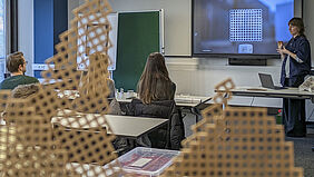 MMM-Präsentation Im Vordergrund steht eine Wabenstruktur auf einem Tisch während im Hintergrund unscharf eine Studentin während der Präsentation zu sehen ist.